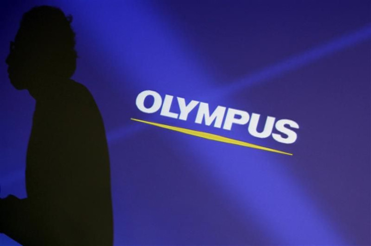 Staff member is silhouetted on a projector screen displaying a logo of Olympus Corp before a news conference in Tokyo
