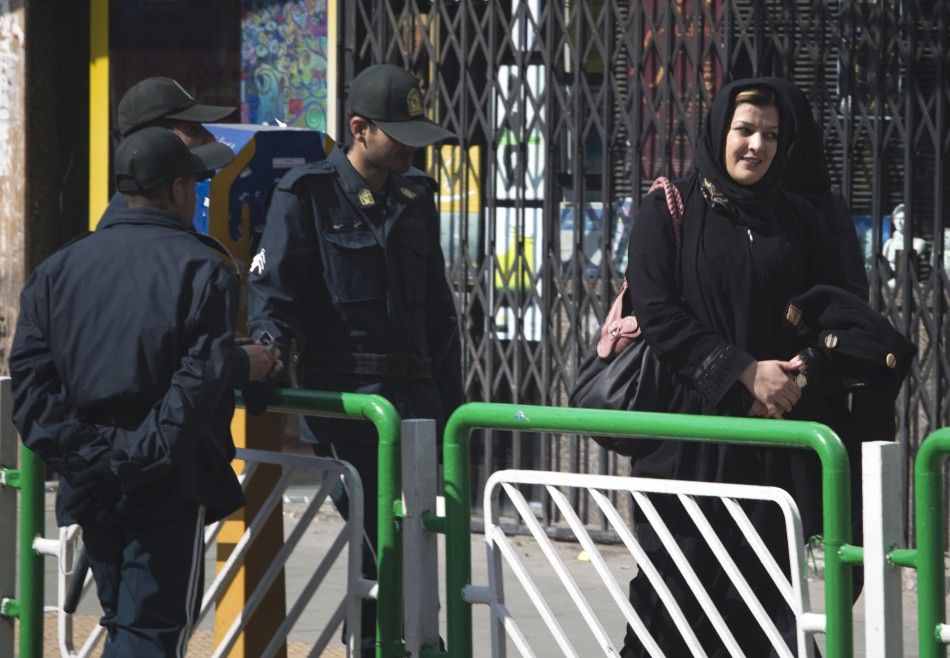 A woman walks past police officers in a square in central Tehran
