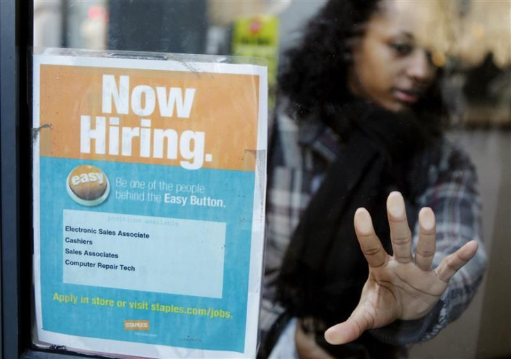 A woman opens a glass door with a &quot;Now Hiring&quot; sign on it as she enters a Staples store in New York