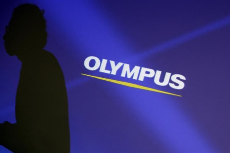 A staff member is silhouetted on a projector screen displaying a logo of Olympus Corp before a news conference in Tokyo February 13, 2012.