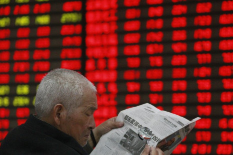 An investor reads a newspaper with a magnifying glass in front of an electronic board showing stock information at a brokerage house in Huaibei, Anhui province April 5, 2012.