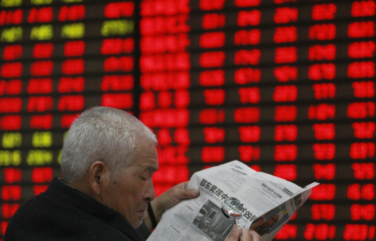 An investor reads a newspaper with a magnifying glass in front of an electronic board showing stock information at a brokerage house in Huaibei, Anhui province April 5, 2012.