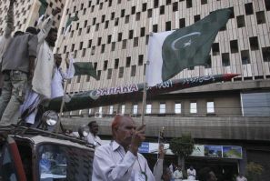 A protestor holds Pakistan&#039;s national flag as others shout slogans while transporting a mock missile during a rally in support of the Pakistan army in Karachi