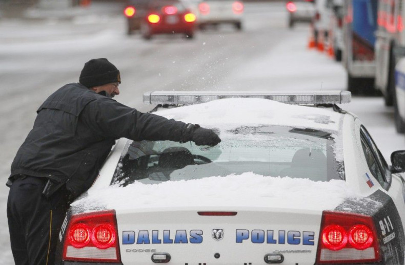 A Dallas police officer removes snow from his car after a storm front moved through Dallas