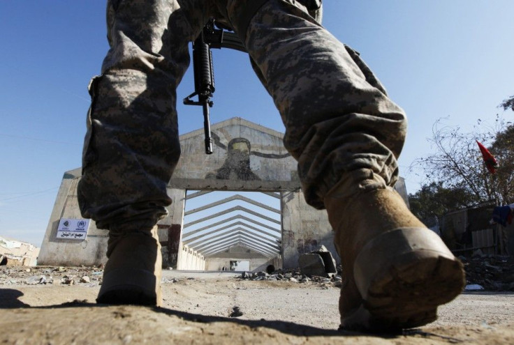 A defaced picture of former dictator Saddam Hussein is seen through legs of a U.S. soldier walking at Umm al-Banin IDP camp