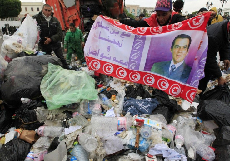 A protester displays a banner of the ousted President Ben Ali found in the garbage, as he helps municipality workers clear up rubbish in Tunis