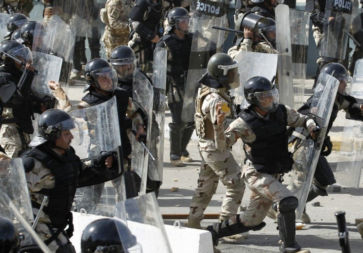 Riot police shield themselves from rocks thrown by protesters during a demonstration in central Baghdad