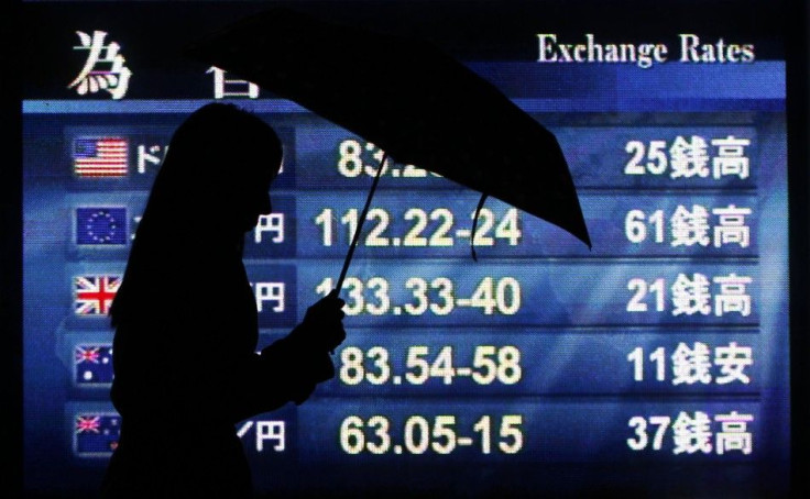 Woman holding an umbrella is silhouetted against a board displaying exchange rates outside a brokerage in Tokyo