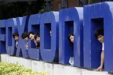 Workers look on from a Foxconn logo near the gate of a Foxconn factory in the township of Longhua, Guangdong province May 29, 2010. 