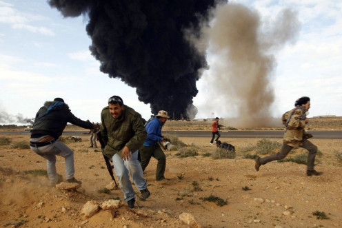 Rebel fighters run for cover in front of a burning gas storage terminal during a battle on the road between Ras Lanuf and Bin Jawad