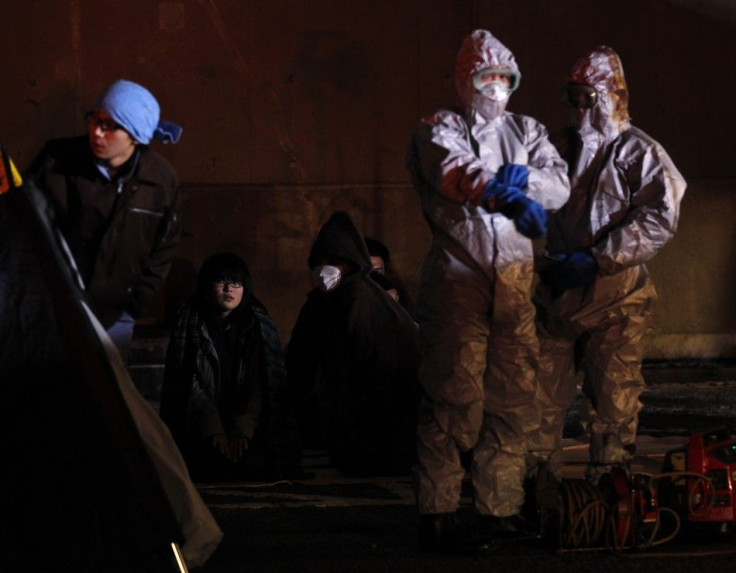 Officials in protective gear stand next to people who are from the evacuation area near the Fukushima Daini nuclear plant, in Koriyama