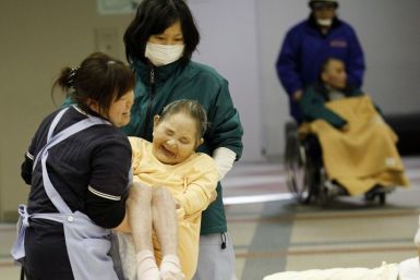 Caretakers carry a woman who is evacuated from a nursing home, which is located in the evacuation area near the Fukushima Daini nuclear plant, at a temporary shelter in Koriyama