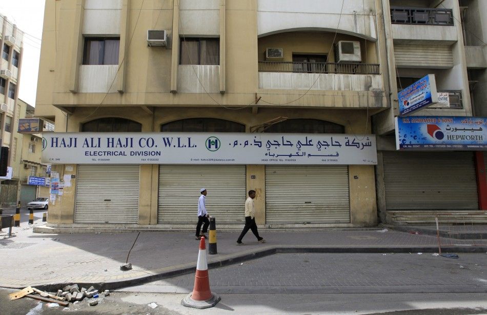 Men walk in front of closed shops near Pearl Square in the center of Manama