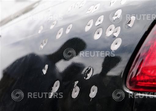 People walk past a car damaged with shotgun pellets in the village of Sitra