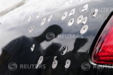 People walk past a car damaged with shotgun pellets in the village of Sitra