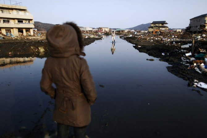 Earthquake and tsunami survivors walk through a flooded street searching for their belongings in the destroyed residential area of Kesennuma
