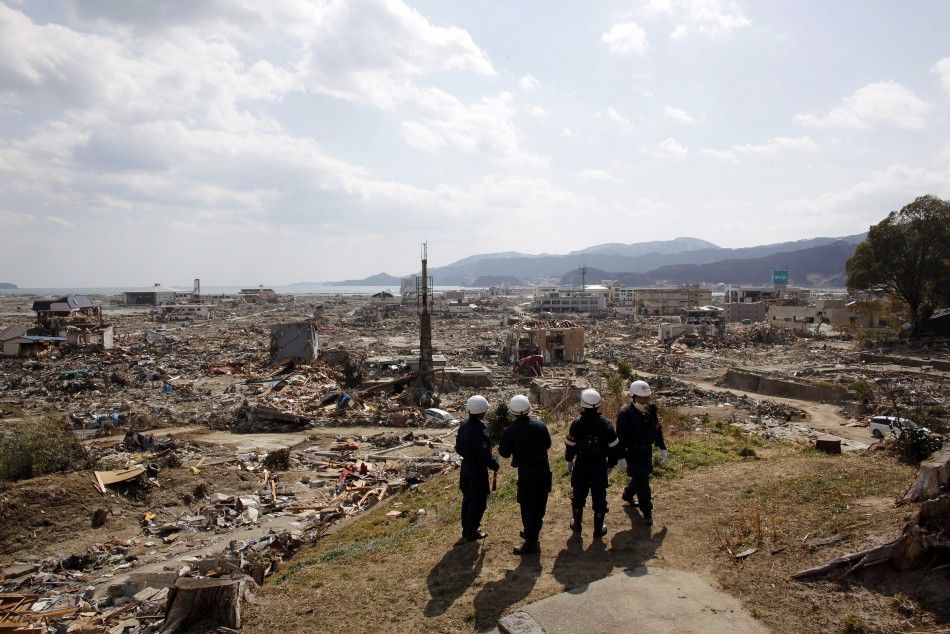 Emergency workers look out from the side of a hill near the debris area near the seaside in Rikuzentakata 