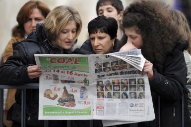Women read a newspaper, with pictures of people killed by the earthquake, in L'Aquila