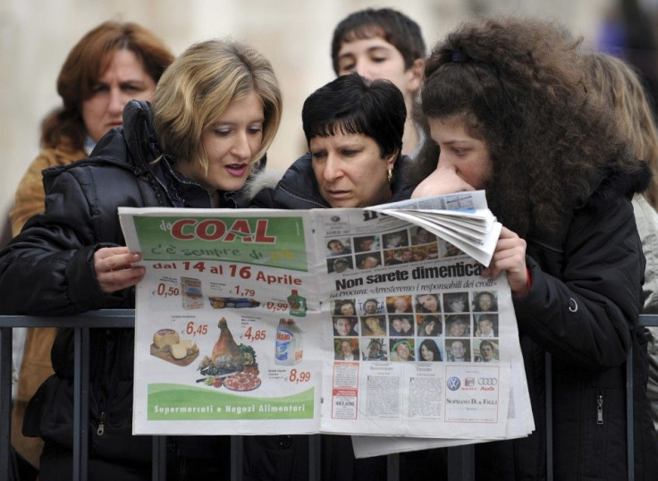 Women read a newspaper, with pictures of people killed by the earthquake, in L'Aquila