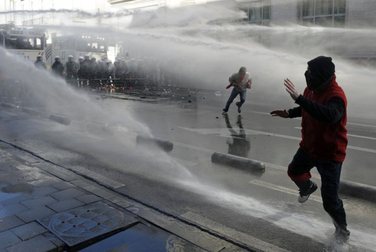 Demonstrators run while being sprayed by water canons during a protest in Brussels