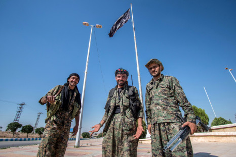People's Protection Units (YPG) fighters stand near an Islamic State flag
