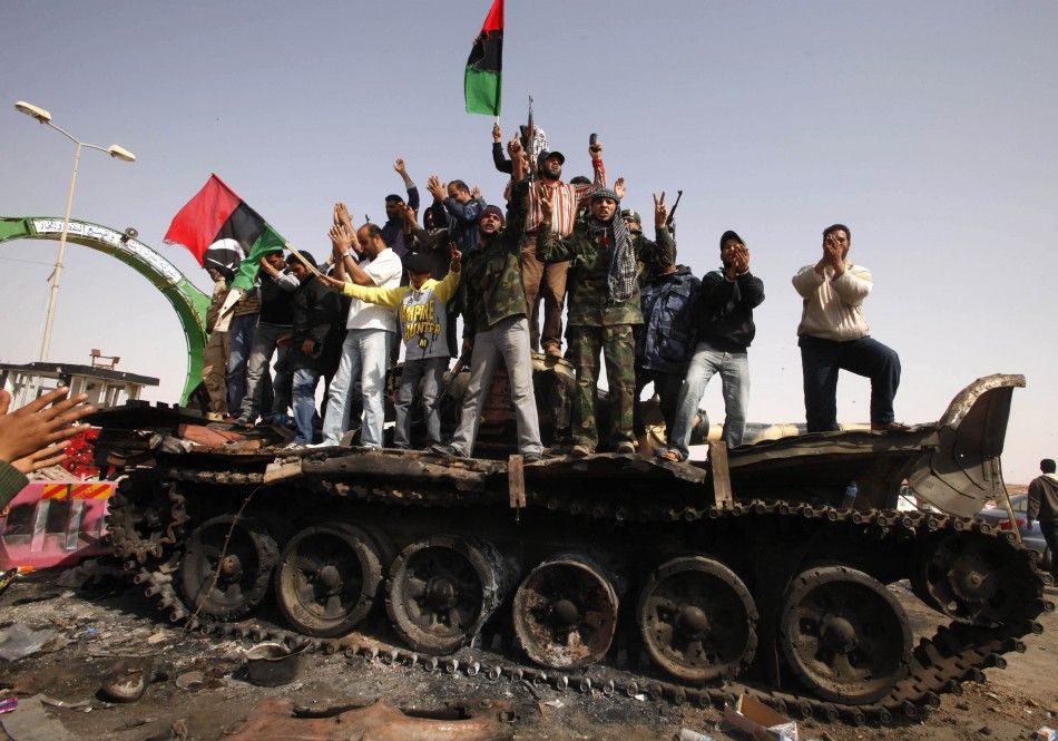 People celebrate atop a destroyed tank belonging to forces loyal to Libyan leader Gaddafi after an air strike by coalition forces in Ajdabiyah 