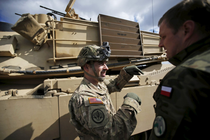 U.S. soldiers in front of a tan colored tank in Europe.