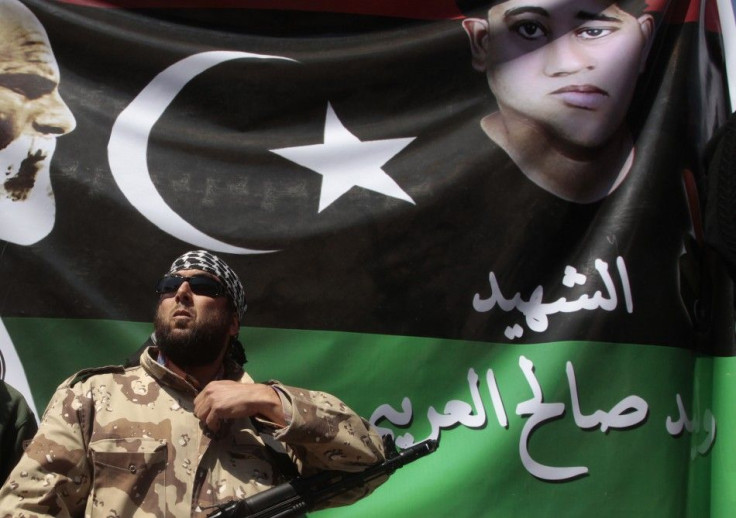A rebel stands guard in front of a picture of a youth killed in the recent clashes, during Friday prayers in Benghazi