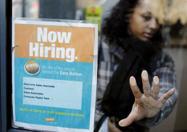 A woman opens a glass door with a "Now Hiring" sign on it as she enters a Staples store in New York