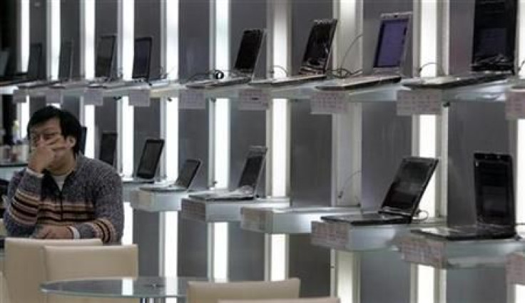 A shop attendant sits in front of a shelf of laptops at a computer store in Taipei