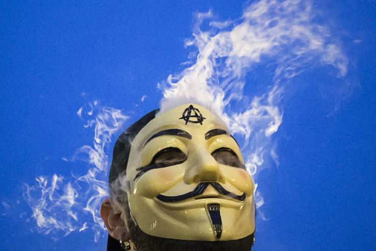 A man smokes behind a Guy Fawkes mask at a protest. 