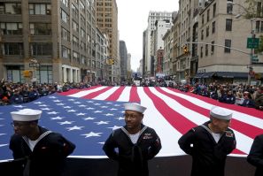 U.S. Navy personnel stand ahead of a U.S. flag during a Veteran's Day parade. 