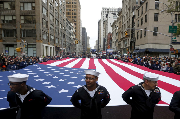 U.S. Navy personnel stand ahead of a U.S. flag during a Veteran's Day parade. 