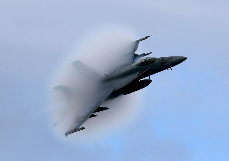 An F/A-18 flies over the USS Eisenhower during maneuvers.  