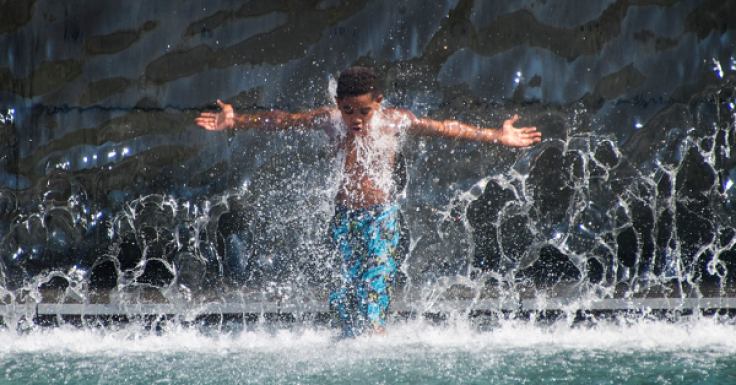 A boy walks through a waterfall on July 25, 2016 while playing in the water at The Yards Park in Washington, DC, as a heat wave rolls across the area