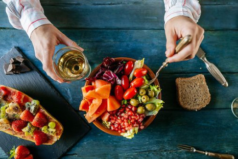 Close-up of woman's hands eating salad wit tomato, pomegranate, papaya and olives, papaya with fruits and with wine glass