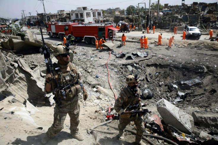 Afghan security forces walk as municipal workers clean up from an attack in Kabul