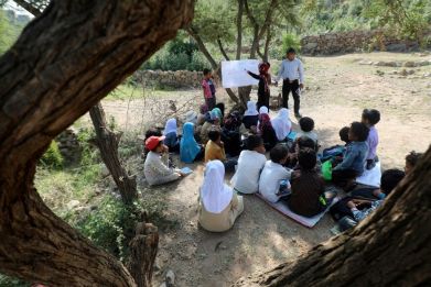 Twenty Yemeni pupils listen to their teacher with textbooks balanced in their laps as they sit under trees in their southern village, where the school building remains unfinished