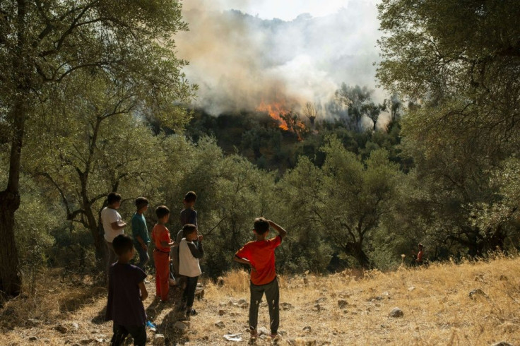 Refugees and migrants look at a fire that broke out in the camp of Moria in Mytilene on September 29, 2019