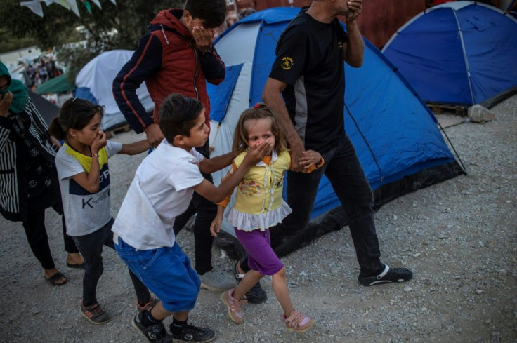 Migrants shield their mouths from tear gas during clashes at the Moira refugee camp