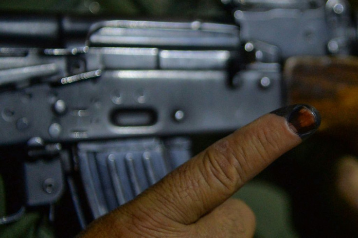 A security guard shows his finger marked with ink as he holds a weapon a day after voting in Afghan presidential elections
