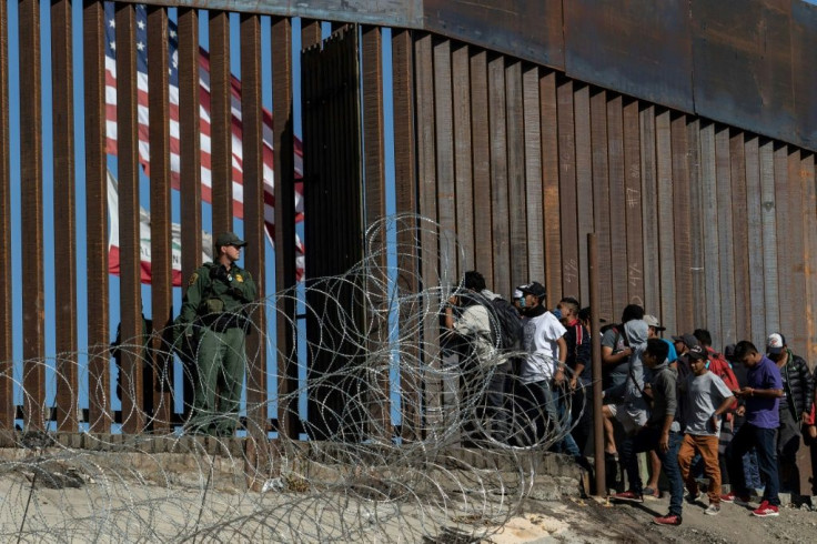 Central American migrants look through a border fence as a US Border Patrol agent stands guard near Tijuana, Mexico: people who cross the border illegally will have their DNA collected by US officials in the future