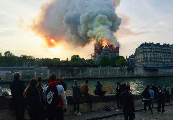 Bystanders look on as flames and smoke billow from the roof of Notre-Dame