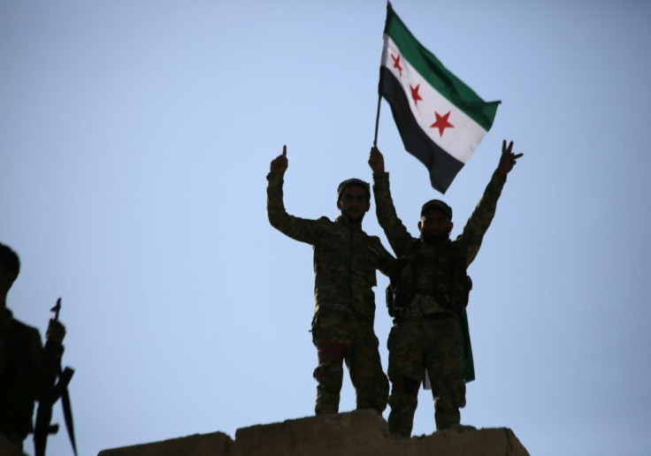 Turkish-backed Syrian fighters wave the Syrian opposition flag on top of a building in the border town of Tal Abyad