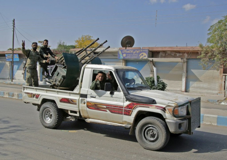 Turkish-backed Syrian fighters ride in the back of a pick up truck in the Syrian border town of Tal Abyad on October 18, 2019