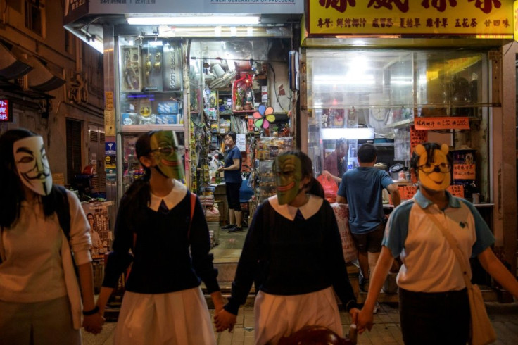 A shopkeeper in Hong Kong watches masked students and protesters gather to form a human chain involving thousands, in opposition to a colonial-era emergency law that bans face masks at demonstrations