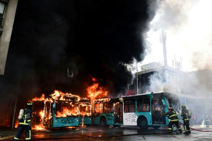 Chilean firefighters extinguish burning buses during clashes between protesters and the riot police in Santiago, on October 19, 2019.Chile's president declared a state of emergency in Santiago Friday night and gave the military responsibility for security