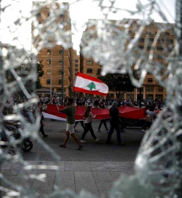 Lebanese demonstrators seen through a damaged shopfront waving a national flag as they take part in a protest in the capital Beirut's downtown district