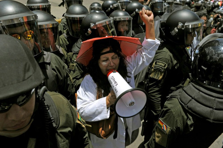 A health worker is surrounded by security forces as she protests outside the headquarters of the election authority in Bolivia's capital La Paz