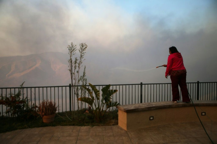 Irene Navarro uses a garden hose to water down vegetation around her property as the Tick Fire burns nearby on October 24, 2019